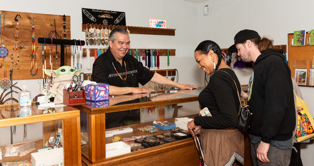 Charlie Stately chats with two customers as they view handmade beaded jewelry in a display case.