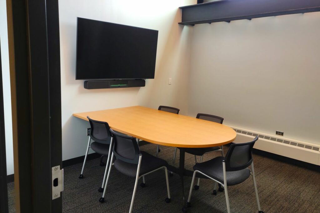 A teleconference room with a large TV screen and office seating.