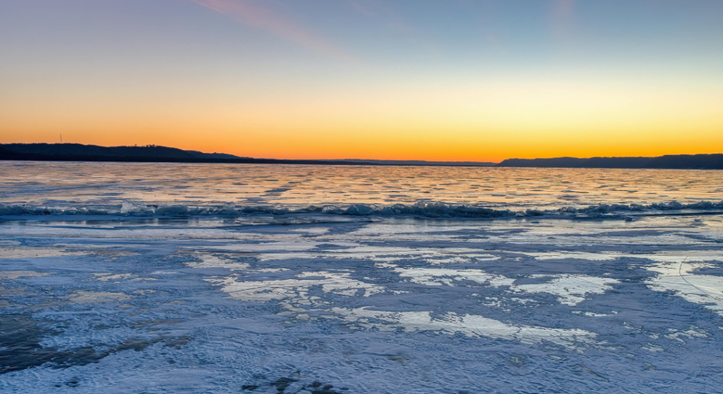 A frozen lake with the sun setting behind it.