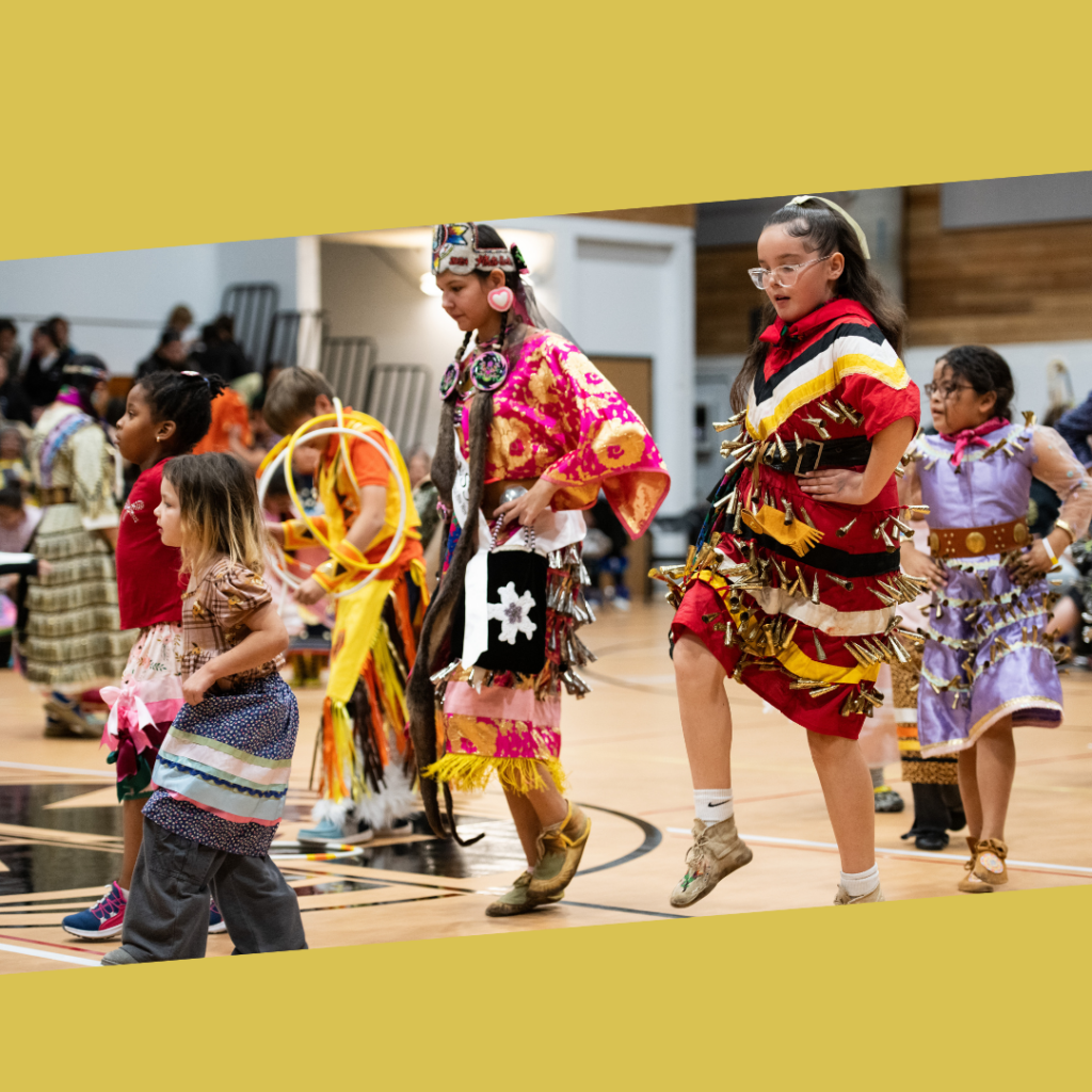 Several children wearing regalia dance at a powwow.
