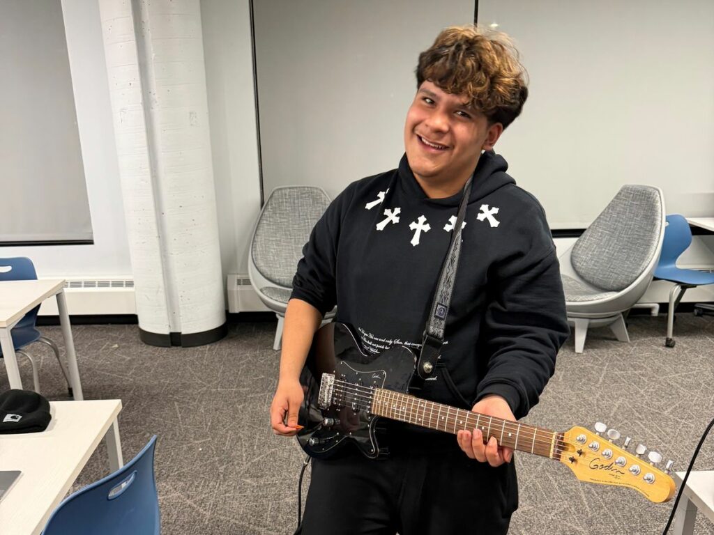 A teen poses for a picture while playing the electric guitar.