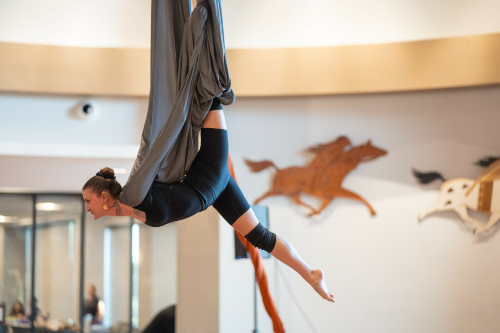 A 20-something Native woman hangs from a ribbon in an aerial fashion.
