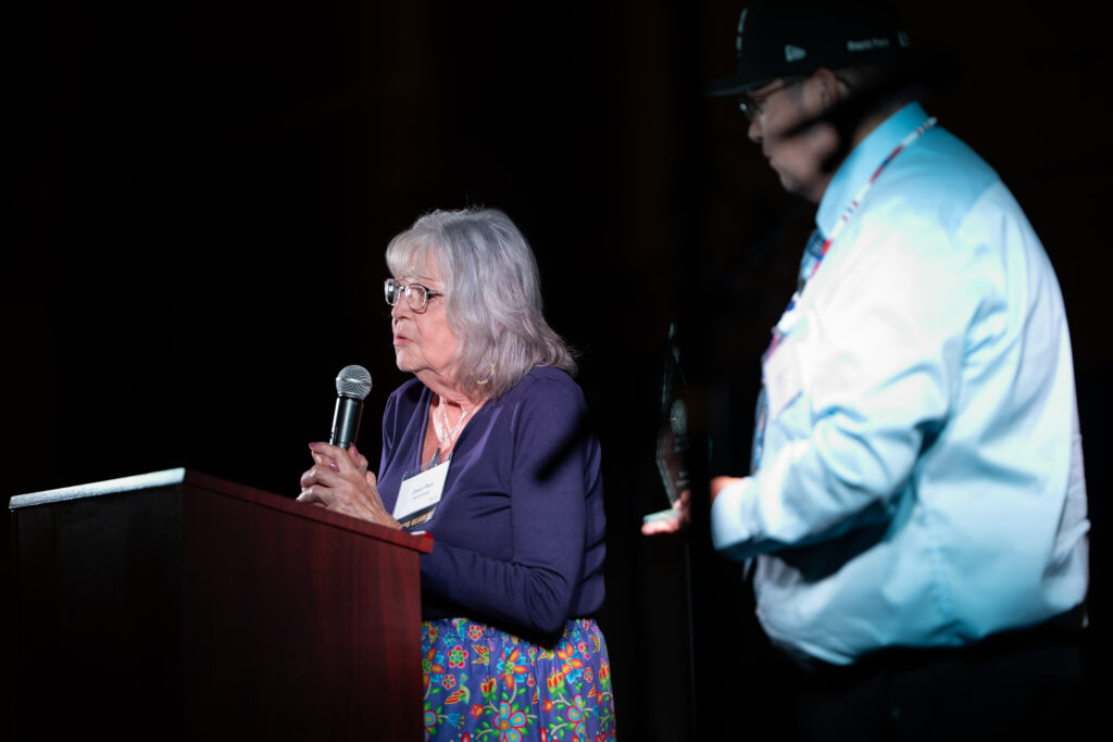 A woman gives a speech at a podium with a handheld microphone.