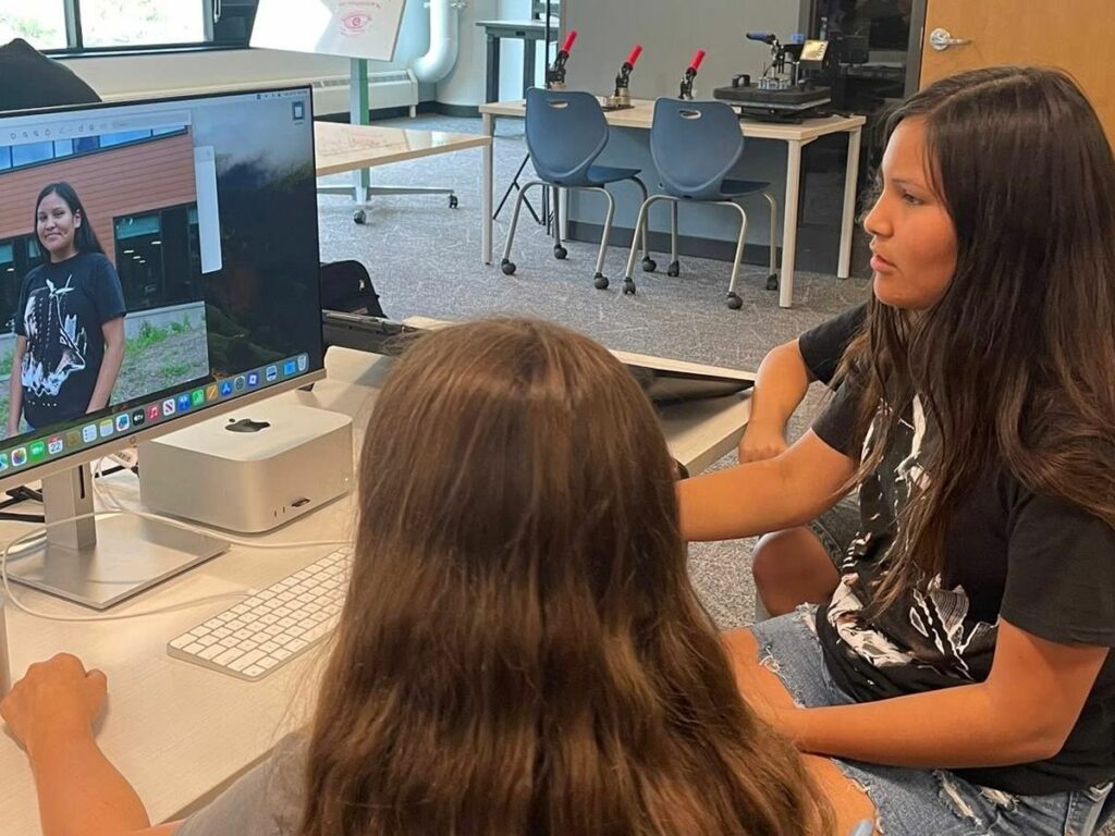 Two teen girls edit a picture on a computer.