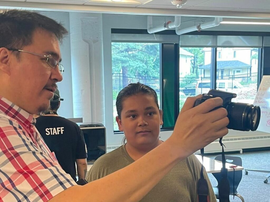 A man shows a teen how to use a digital camera.